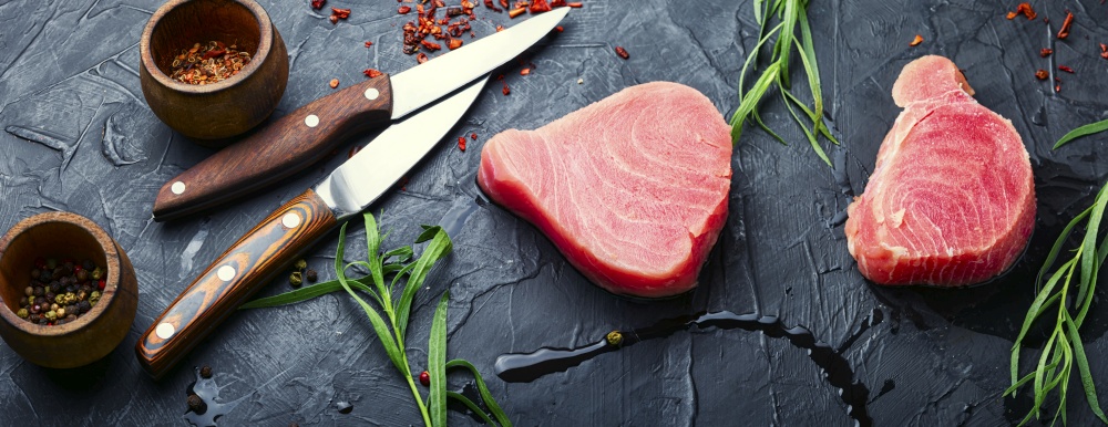 Fresh raw tuna steak and tarragon on kitchen table. Raw tuna fish