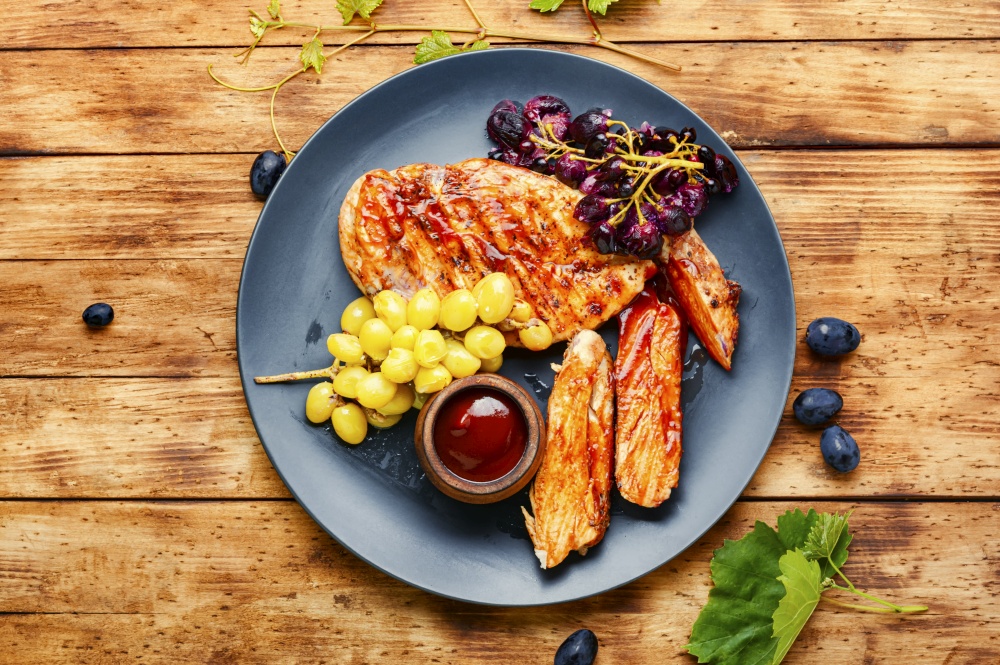 Sliced chicken breast with grapes on rural wooden table. Sliced grilled chicken breast