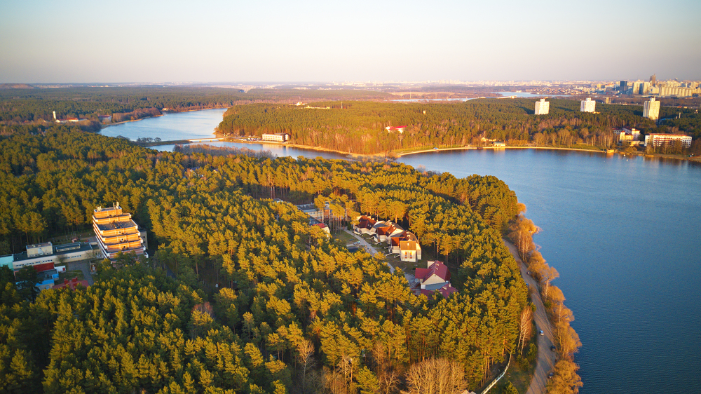 Recreation zone and big city aerial view. Riverbank with forest and sanatorium in spring sunlight. April evening at the lake near Minsk, Belarus. Beautiful sunset panoramic scene.