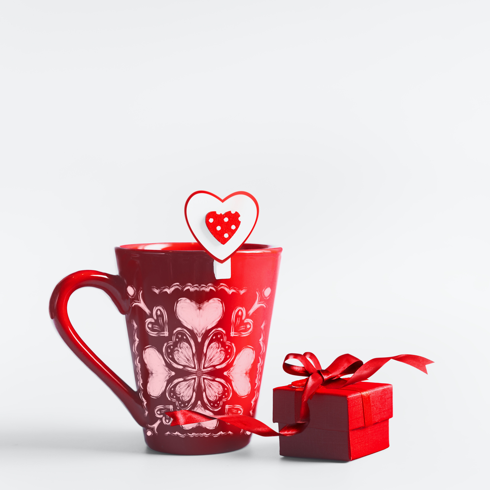 Red mug with hearts and gift box with ribbon standing on white background. Declaration of love and Valentines day concept