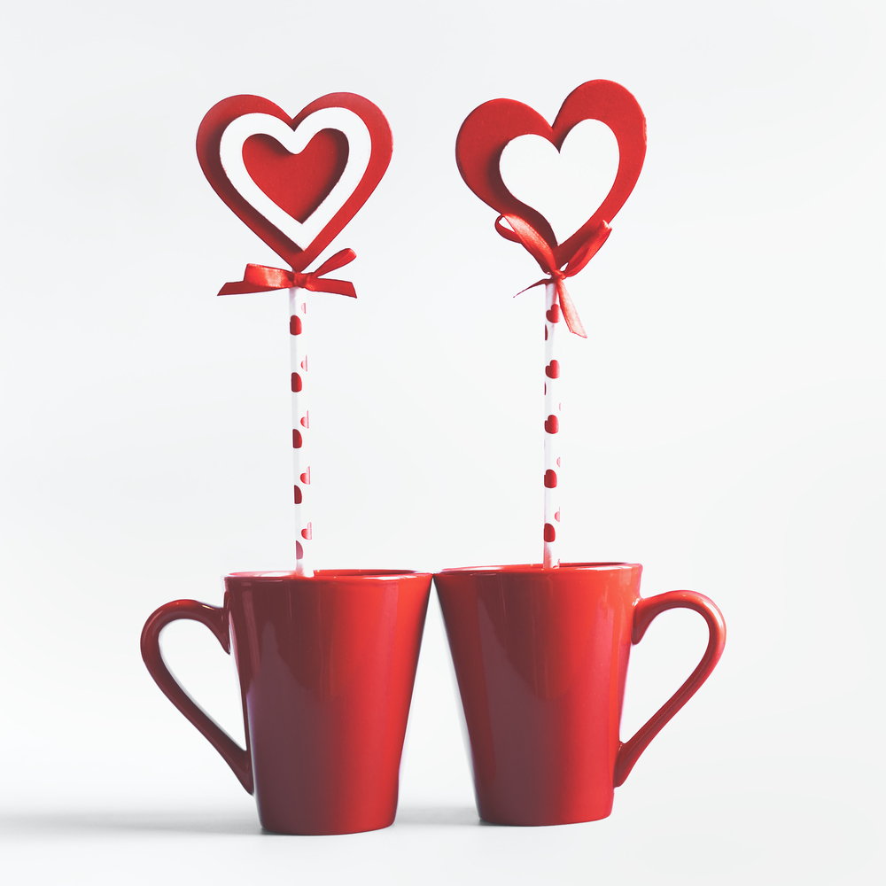 Two red mugs with hearts lollipop standing on white background. Declaration of love and Valentines day concept