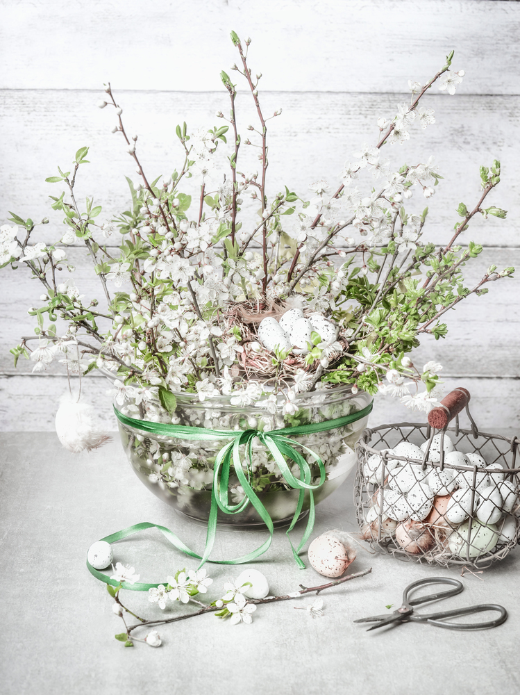 Bunch of spring blossom twigs in vase with Easter eggs on white table. Still life . Easter decorations making
