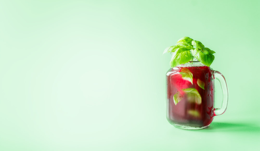 Red berries lemonade in Mason jar  flavored with herb leaves at sunny bight mint green background. Summer mood.  Healthy drinks and lifestyle. Copy space