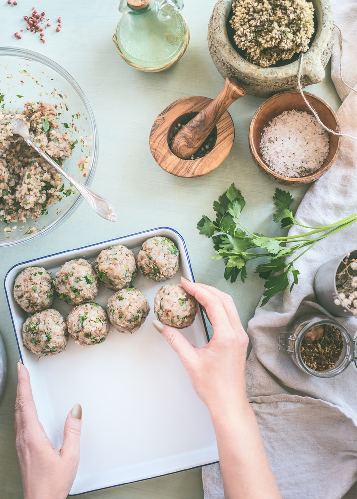 Female hand make buckwheat balls on kitchen table background with herbs and spices, top view. Healthy homemade food