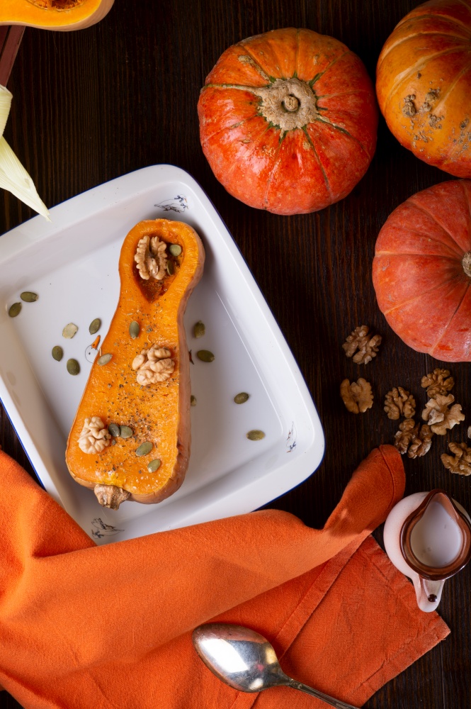 baked pumpkin with walnuts and seeds,  coconut milk  served at wooden brown table with ripe orange  pumkins. flat lay. healthy life concept