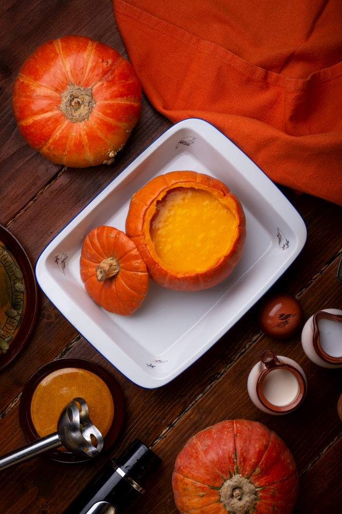 baked pumpkin cream coup served in pumpkin. served at wooden brown table with ripe orange  pumkins. flat lay. healthy life concept