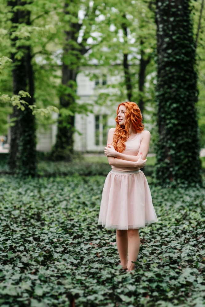 red-haired young girl walking in a park between trees and architectural objects