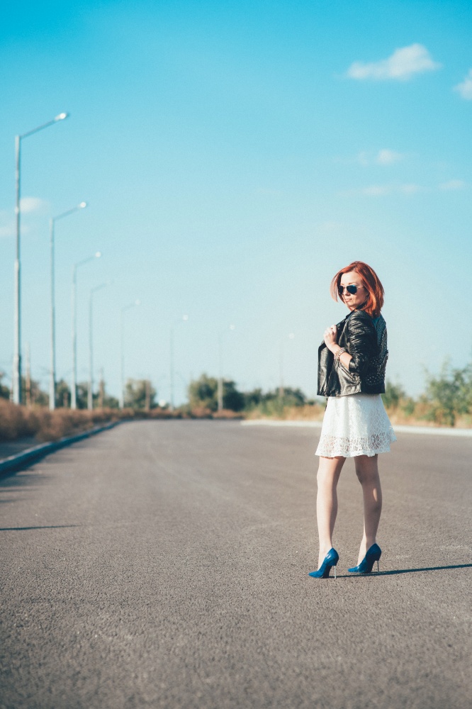 red-haired girl in a black jacket and blue glasses on a gray road