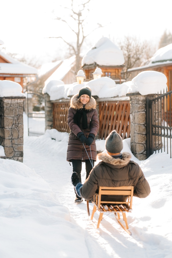 girl carries a guy on a sled on a snowy street on a sunny day