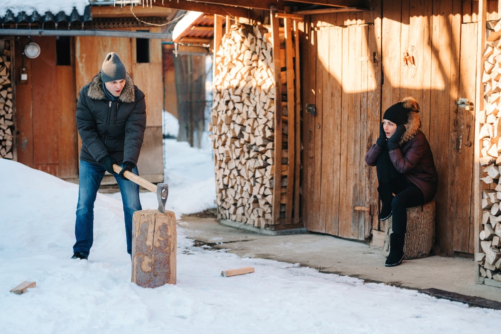 guy in winter clothes chopping wood in the yard, covered with snow