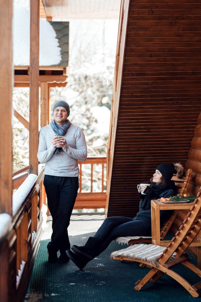 couple of young people a guy and a girl on the porch of a snow-covered wooden house in the winter mountains
