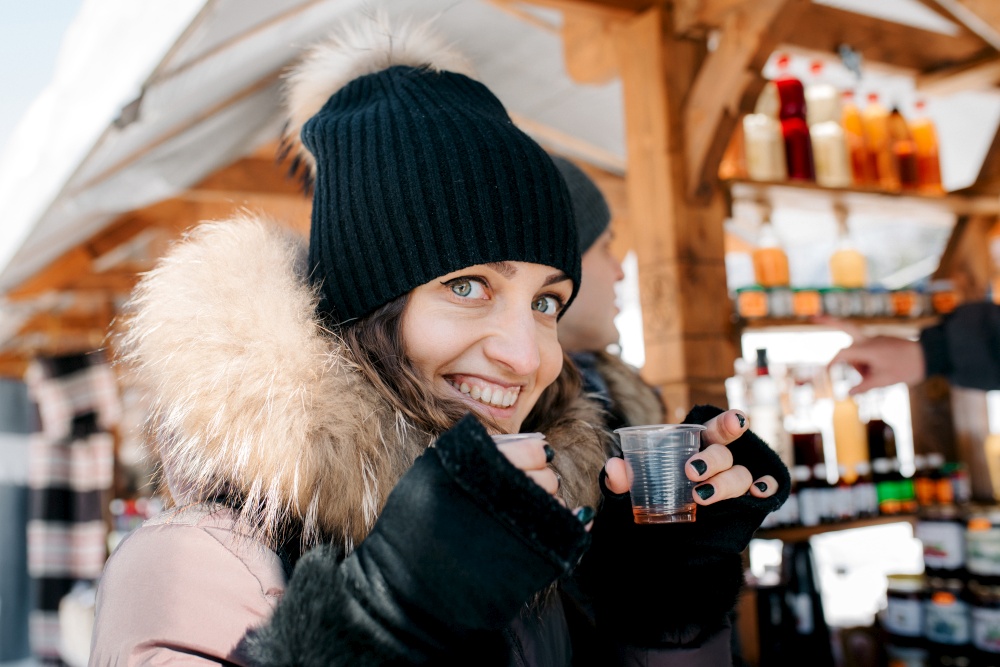 joyful girl in warm winter clothes at the market try drinks