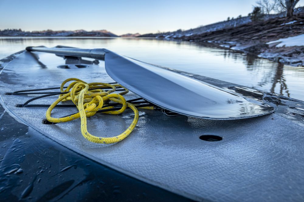 Winter dusk after paddling workout - yellow rope and paddle on an icy deck of stand up paddleboard, Horsetooth Reservoir in northern Colorado