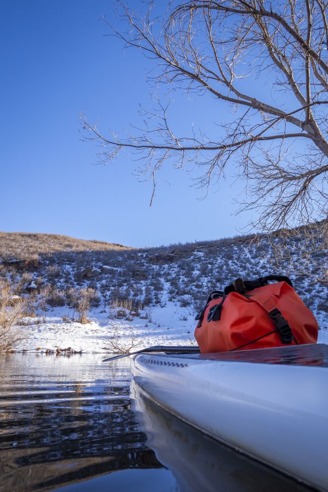 stand up paddleboard with a dry bag on a deck, winter scenery on a mountain lake, POV from an action camera