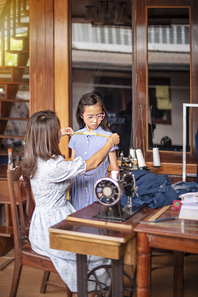 asian tailor working with measuring tape, dressmaker measuring girl in workroom. Beautiful asian dressmaker in workroom