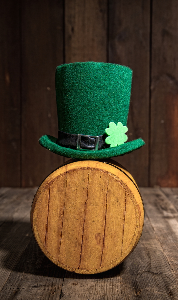 Green leprechaun hat stands on a small wooden barrel with beer in an Irish pub for St. Patrick&rsquo;s Day.. Leprechaun hat barrel