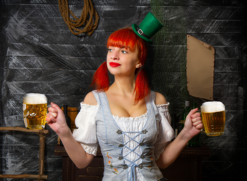 young red-haired Irish waitress in a little leprechaun hat brings two glasses of foamy beer in a St. Patrick&quot;s Day pub. Irish waitress beer