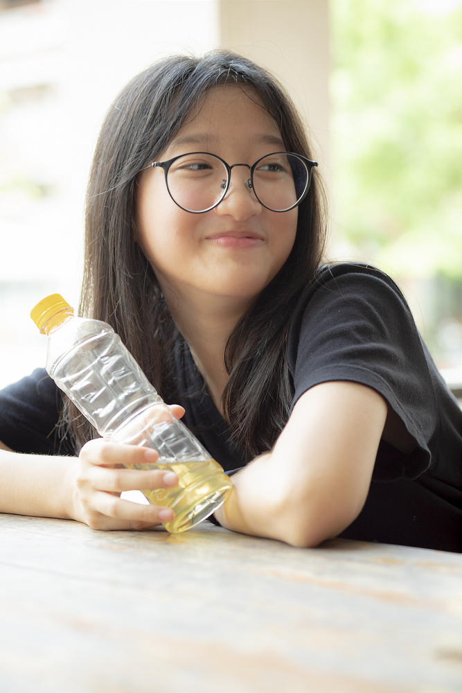 asian teenager smiling face holding pastic bottle in hand