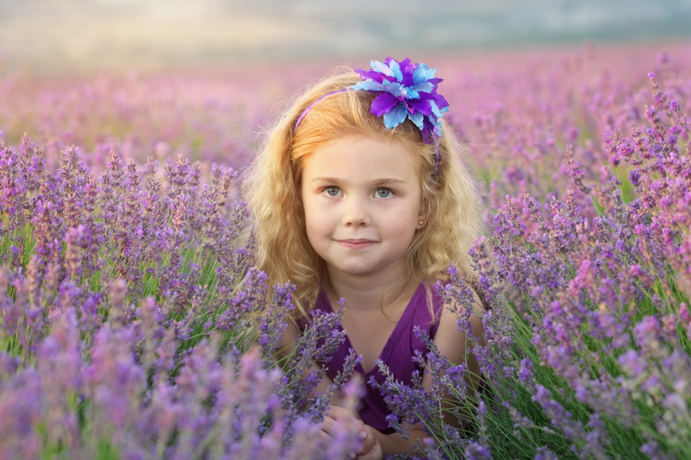 Cute little girl sitting at lavender meadow. Portrait and nature composition.