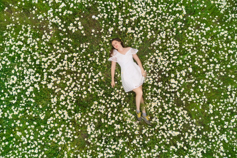 Beautiful girl lies in camomile daisy flower. View from above. Aerial photography.