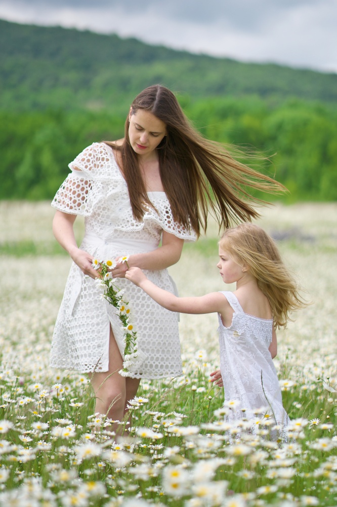 Happy mother and daughter making wreath in big camomile mountain meadow. Emotional, love and care scene.
