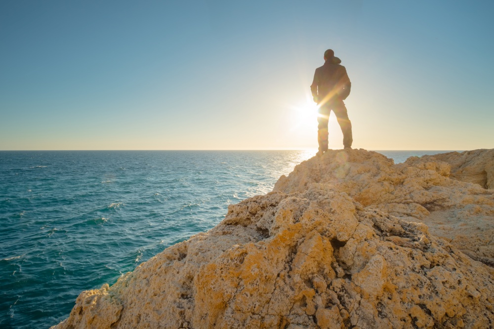 Man stands on the edge of the abyss and looks at the sea. Man relax on nature.