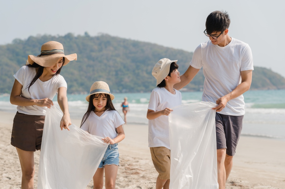 Asian young happy family activists collecting plastic waste and walking on beach. Asia volunteers help to keep nature clean up garbage. Concept about environmental conservation pollution problems.