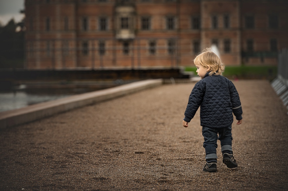 Little boy is walking on a dirt road to an old building