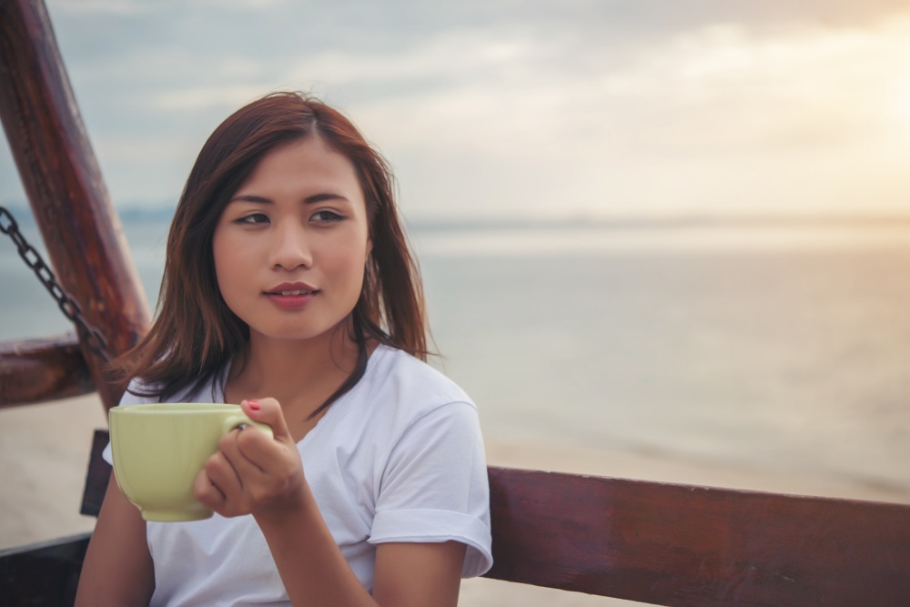 Beautiful woman drink coffee while sitting on swing on the beach.