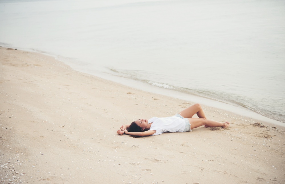 Young woman with white t-shirt lying down on the beach. Smiling enjoy with natural. Women lifestyle concept.