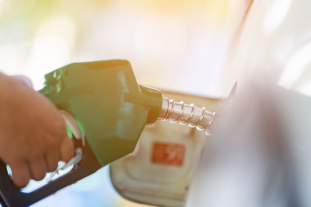 Man Handle pumping gasoline fuel nozzle to refuel. Vehicle fueling facility at petrol station. White car at gas station being filled with fuel. Transportation and ownership concept.