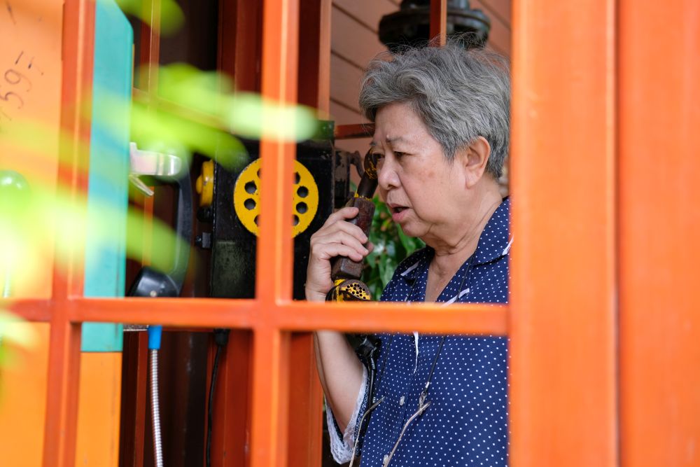 old elderly senior woman talking on vintage public telephone booth