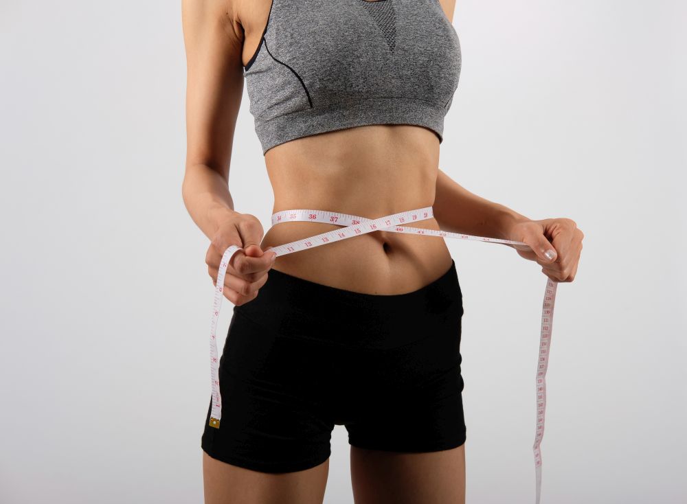 sporty fitness woman in sportswear with measuring waist with tape on white background. healthy sport lifestyle