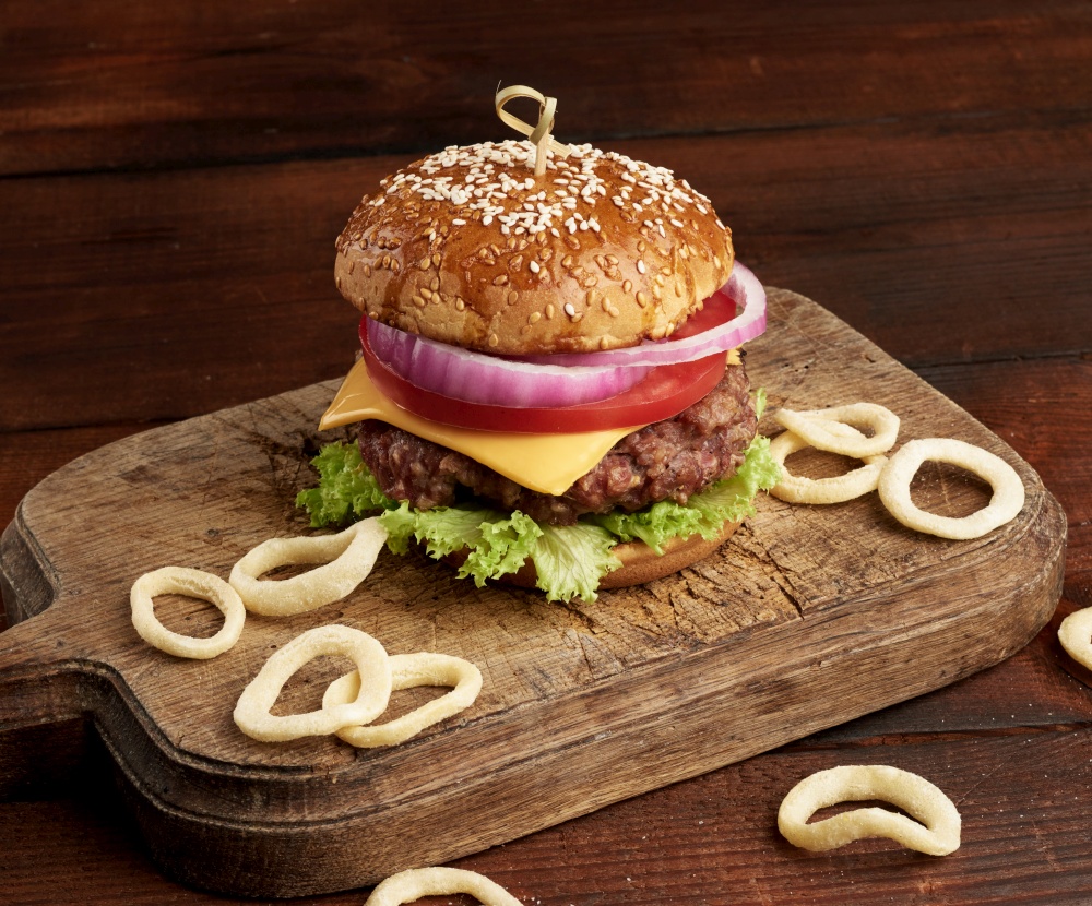 delicious burgers with fried beef cutlet, tomato, lettuce and onions, crispy white wheat flour bun with sesame seeds. Fast food on a wooden board, top view