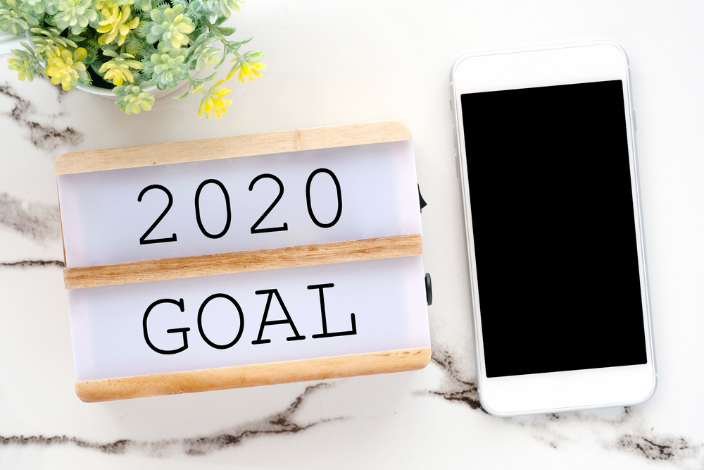 2020 goal on wood box and smart phone with blank screen on white marble background, new year aim to success in business background