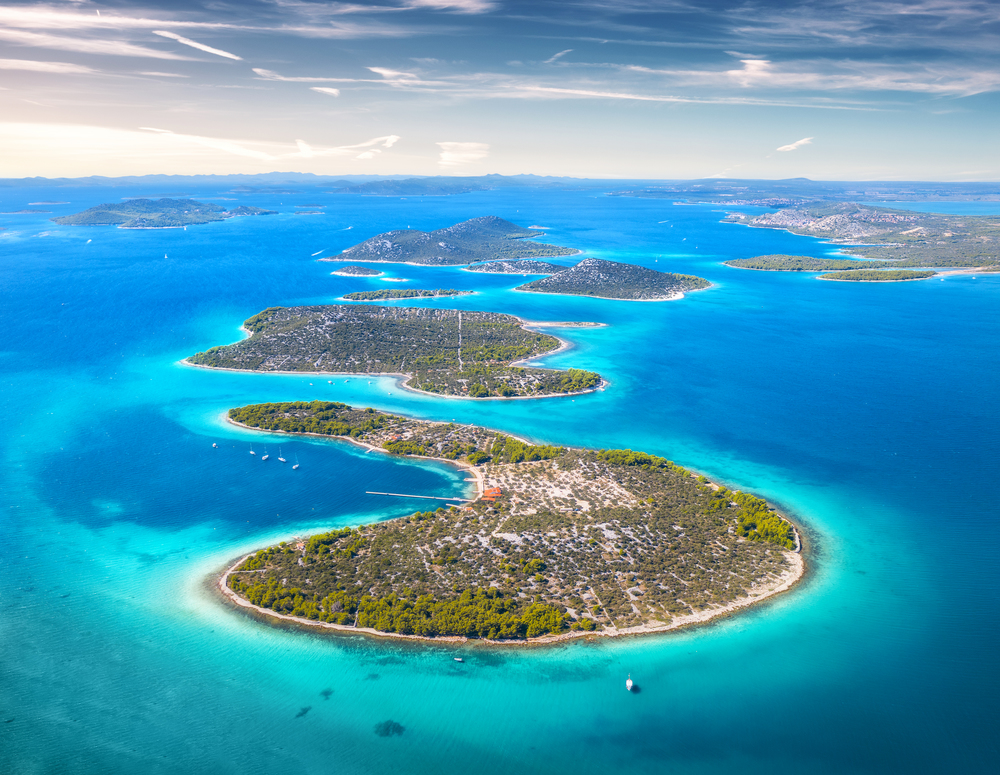 Aerial view of beautiful small islands in Adriatic sea at sunny day in summer in Croatia. Top view of transparent blue water, green trees, mountain, sandy beach, boats and yachts. Tropical landscape