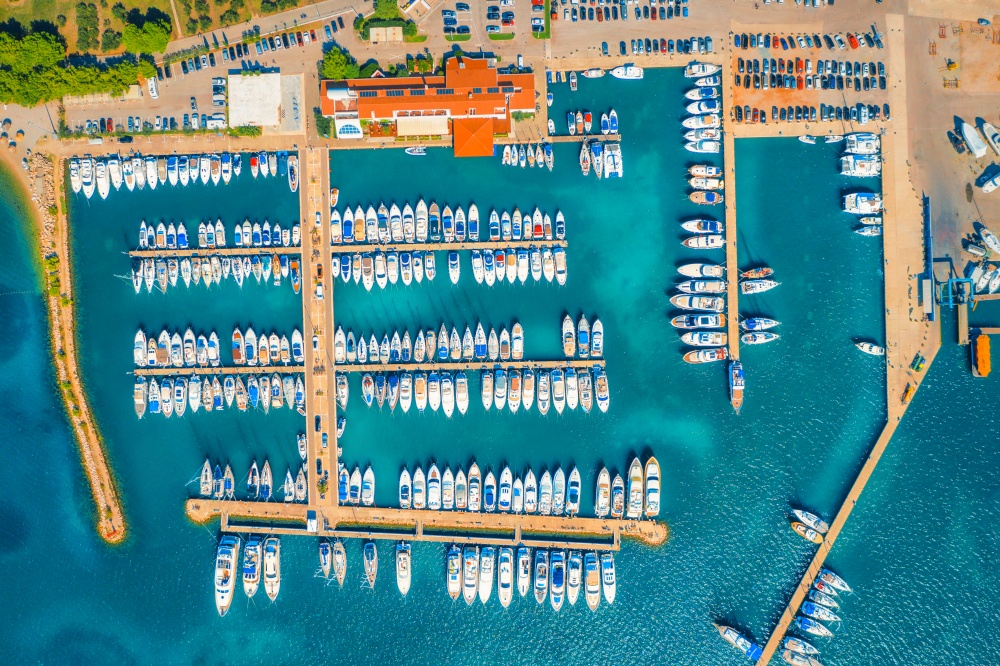 Aerial view of boats and yachts in port in beautiful old city at sunset in Croatia in summer. Landscape with buildings with orange roofs, motorboats in harbor, clear blue sea, cars, road. Top view