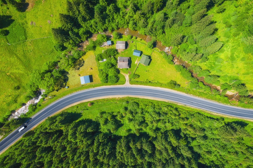 Aerial view of road in beautiful green forest at sunset in summer. Colorful landscape with roadway, pine trees. Carpatian mountains. Top view from drone of highway. View from above. Travel in Ukraine