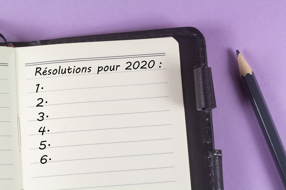 Notebook with 2020 resolutions in french language and pencil on purple background