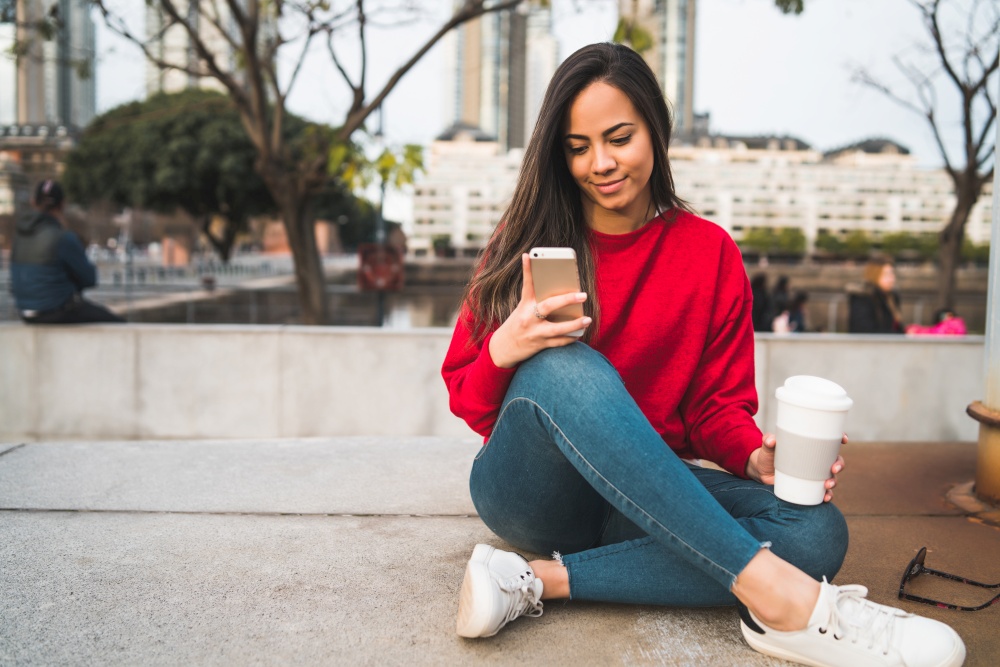 Portrait of young beautiful woman using her mobile phone while sitting outdoors. Communication concept.