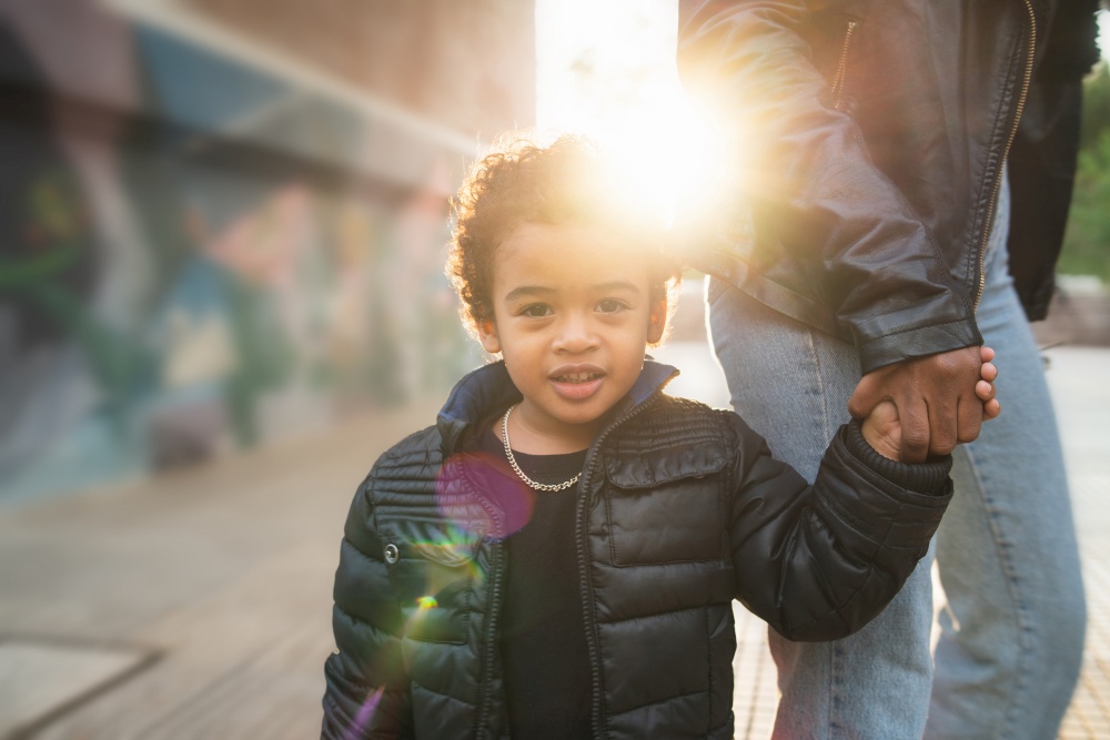 Portrait of cute african american little boy outdoors in the street holding his mother&rsquo;s hand.