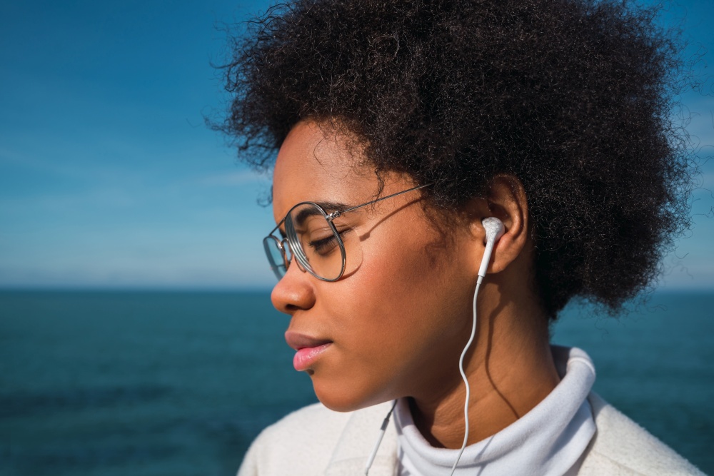 Portrait of young latin woman listening to music with earphones with the sea on background. Music, lifestyle.