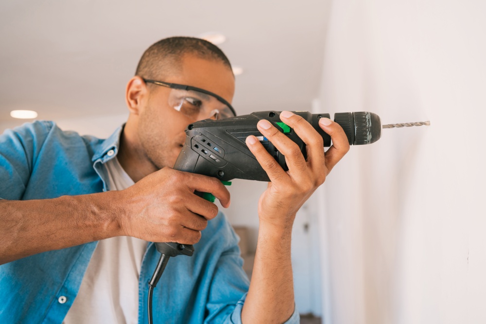 Portrait of young latin man with a electric drill and making hole in wall. Interior design and home renovation concept.