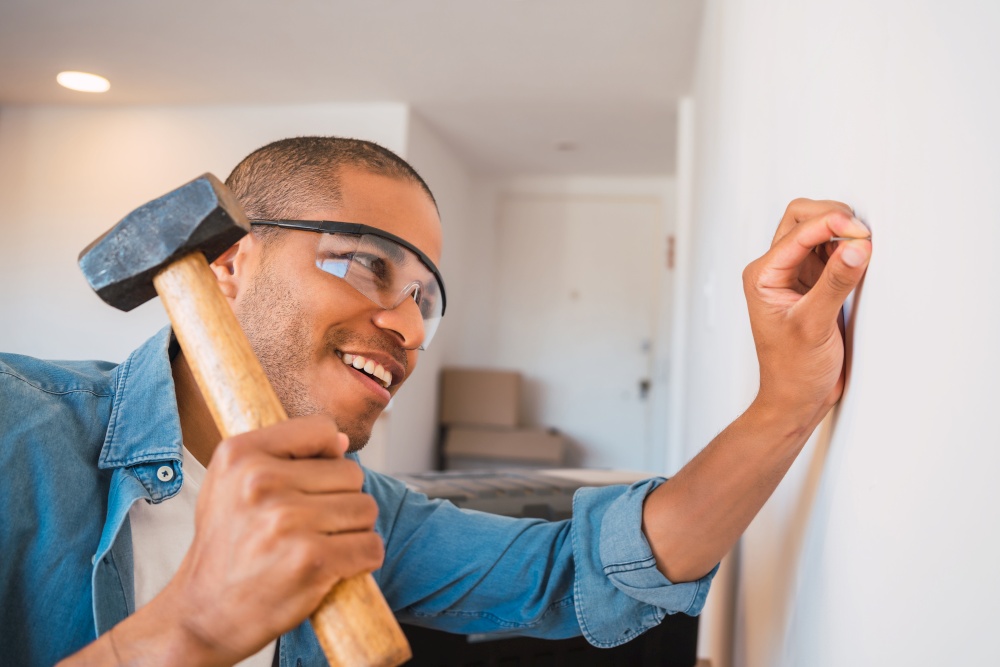 Portrait of young latin man hammering nail on the wall at home. Home improvement and repair home concept.