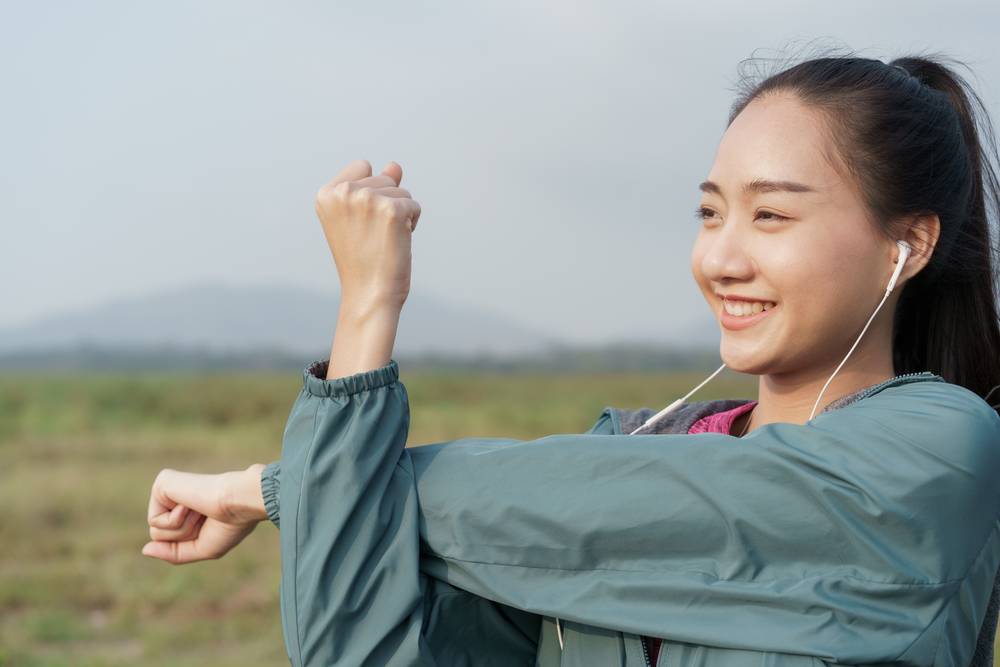 Medium Close- up Asian girl smile on the face, sports women preparing for a workout at outdoor on mountain background in the summer, Woman stretching arms or warming-up, Concept exercise wellness