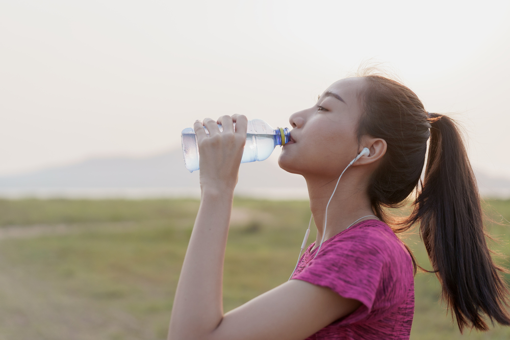Side view of Asian fitness athlete women with drink bottle water and relax after a workout or running in the summer at sunset or sunrise. Concept wellness and lifestyle