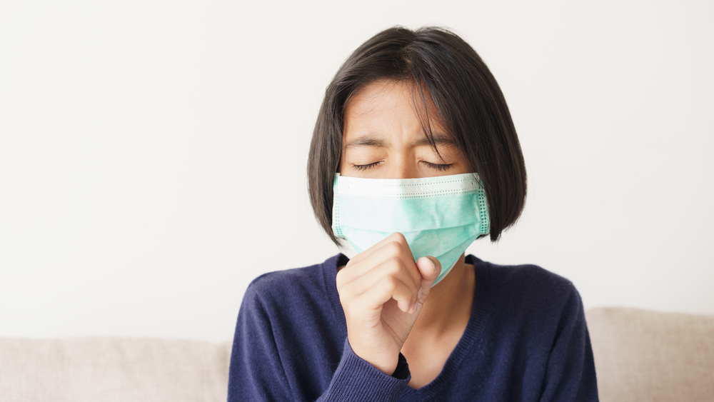 Asian girl symptom cough and are protective with medical mask while sitting on sofa, Asia child wearing a protection mask epidemic of flu or covid-19 in living room at home. Health and illness concept