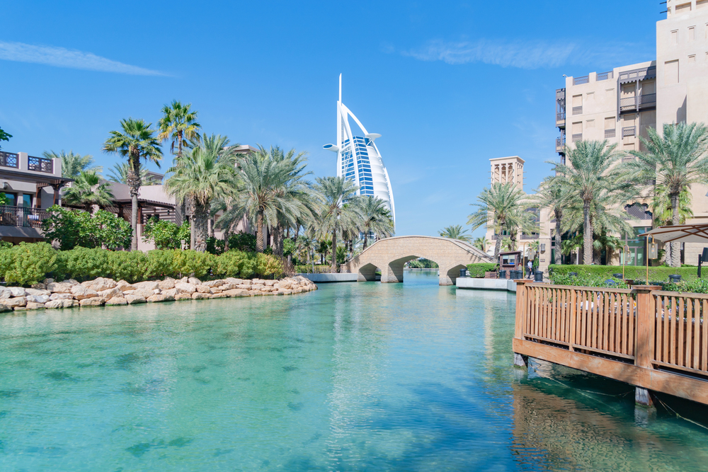 Burj Al Arab Jumeirah Island or boat building with turquoise lake or river and reflection, Dubai Downtown skyline, United Arab Emirates or UAE. Hotel in urban city at noon in travel vacation concept.