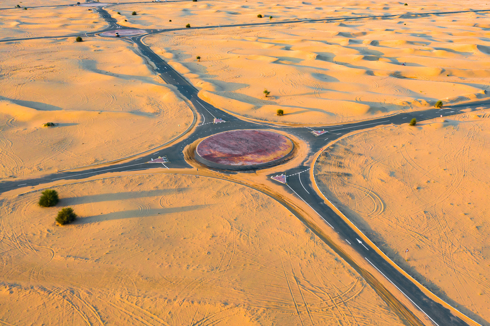 Aerial view of circle roundabout, half desert road or street with sand dune in Dubai City, United Arab Emirates or UAE. Natural landscape background at sunset time. Famous tourist attraction.