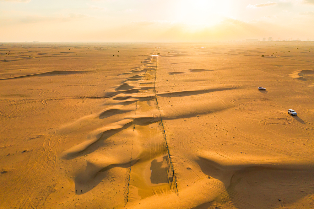 Aerial view of half desert road or street with sand dune in Dubai City, United Arab Emirates or UAE. Natural landscape background at sunset time. Famous tourist attraction. Top view.
